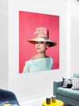 Audrey Hepburn portant un grand chapeau de paille et un nœud rose sur fond rose.