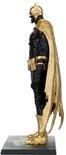 Profiel van een actiefiguur van Batman in een zwart pak met gouden details, gouden kap en gouden gescheurde cape, staand op een zwarte sokkel.