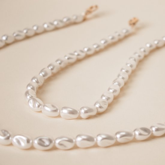 Close-up van een lange, witte parelketting met onregelmatige, gladde parels.