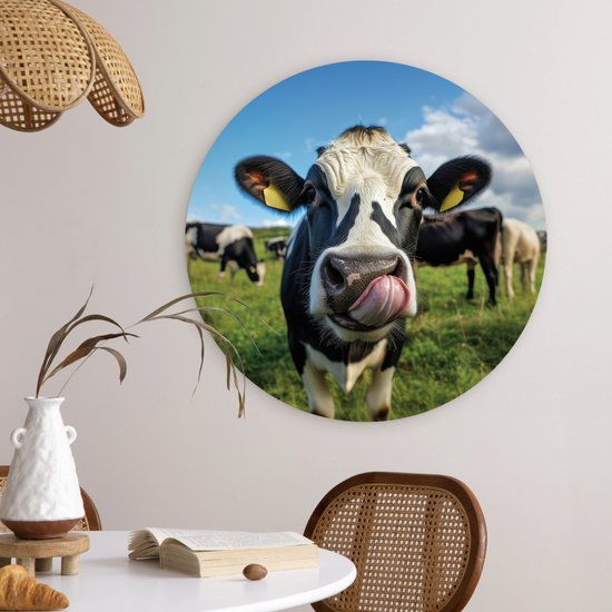 Ronde muurdecoratie van een Holstein koe die met haar tong likt, boven een eettafel in een woonruimte.