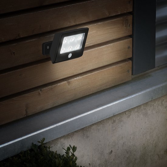 Zwarte LED buitenlamp gemonteerd op een houten muur, verlicht de omgeving.