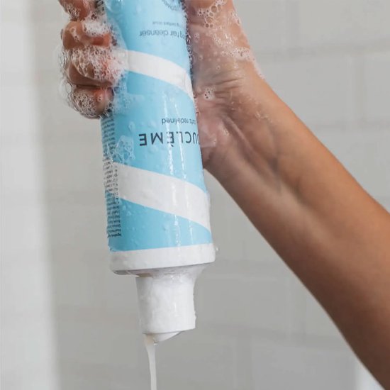 Hand houdt een fles hydraterende haarreiniger vast met blauwe en witte strepen, druppels en schuim.