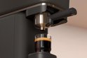 Zwarte Philips Baristina volautomatische espressomachine met een glas espresso.