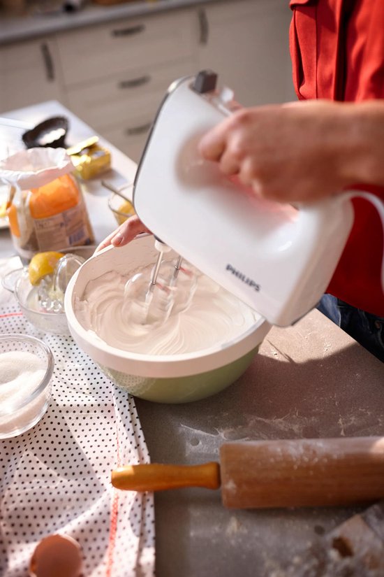 Handen gebruiken een witte Philips handmixer om eiwitten te kloppen in een kom.