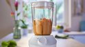 Witte Philips blender met kan gevuld met bruine substantie. Zijaanzicht.