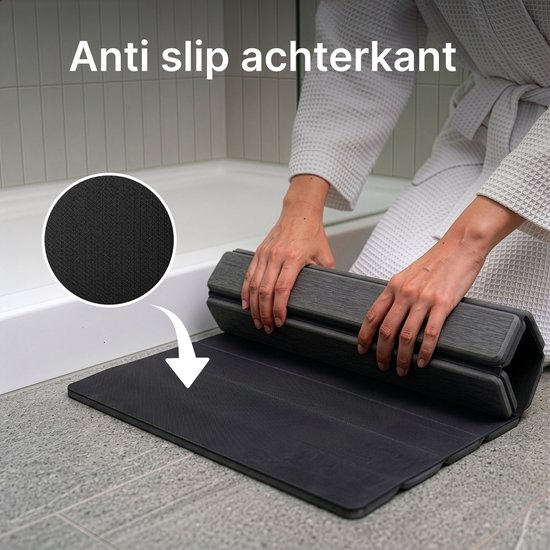 Een donkergrijze badmat wordt uitgerold; de onderkant is antislip en de mat droogt snel.