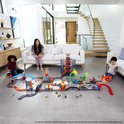 Deux enfants jouent avec un ensemble de piste de course Hot Wheels élaboré dans un salon.