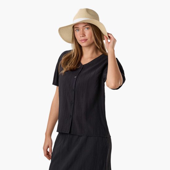 Model in zwarte blouse met knoopjes en strooien hoed met wit lint, houdt hoed vast.