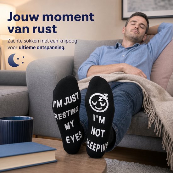 Man op een bank met zijn ogen dicht, draagt zwarte sokken met de tekst 'I'M JUST RESTING MY EYES' en 'I'M NOT SLEEPING'.