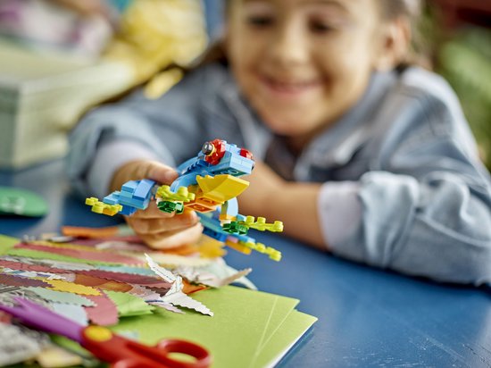 Een meisje houdt een kleine blauwe en gele LEGO-kikker met rode oogjes vast.
