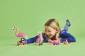 Meisje met roze LEGO flamingo, papegaai en zeepaardje, lachend op een groene ondergrond.