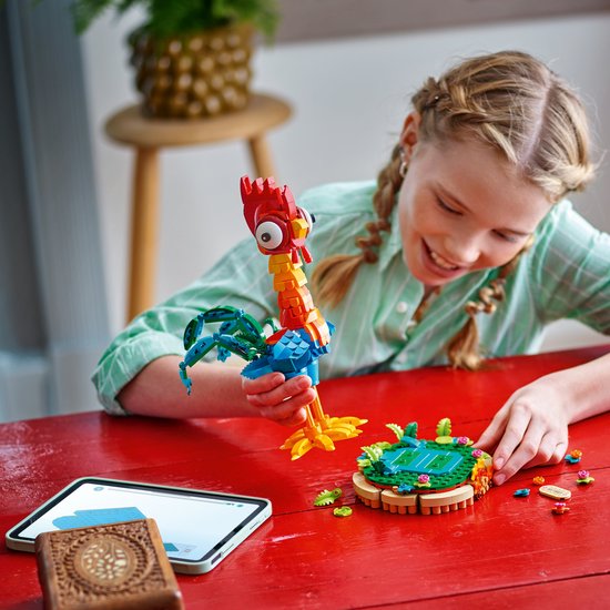 Une fille construit la figurine Heihei avec des LEGO, avec une tête rouge et des ailes et une queue bleu-vert.