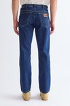 Model van achteren, draagt een donkerblauwe jeans en beige instappers.