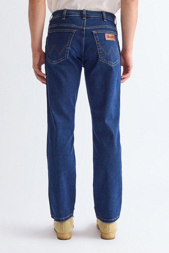 Model van achteren, draagt een donkerblauwe jeans en beige instappers.