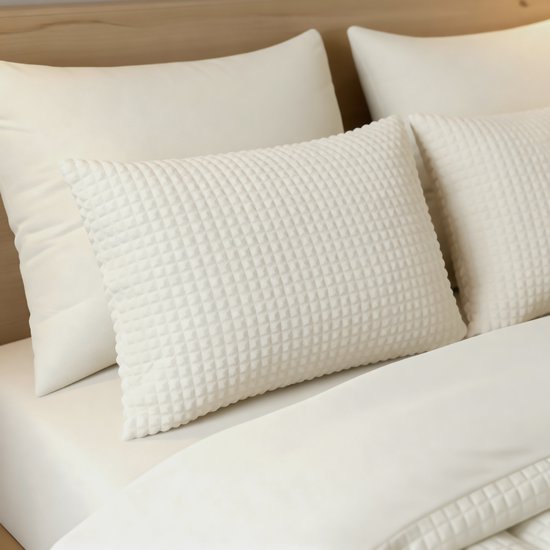 Crème teddy check kussensloop op een bed met witte lakens.