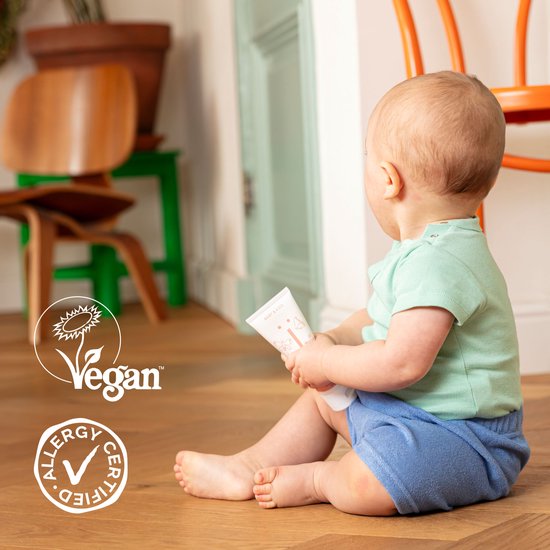 Baby zit op de grond en houdt een flesje Naïf babypoeder vast. Vegan en Allergy certified logo's.