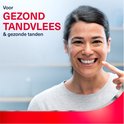Vrouw met donker haar lacht en wijst naar haar mond. Tekst: Voor gezond tandvlees & gezonde tanden.