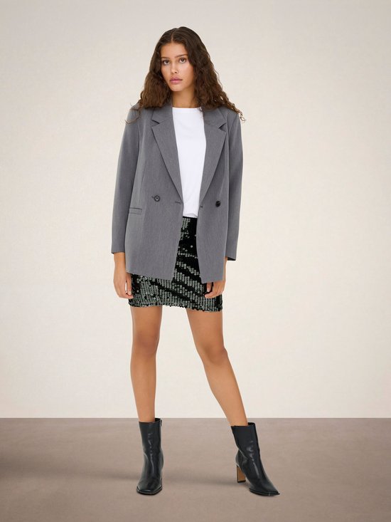 Model met een zwarte pailletten minirok met grafische pailletten, en een grijze blazer.