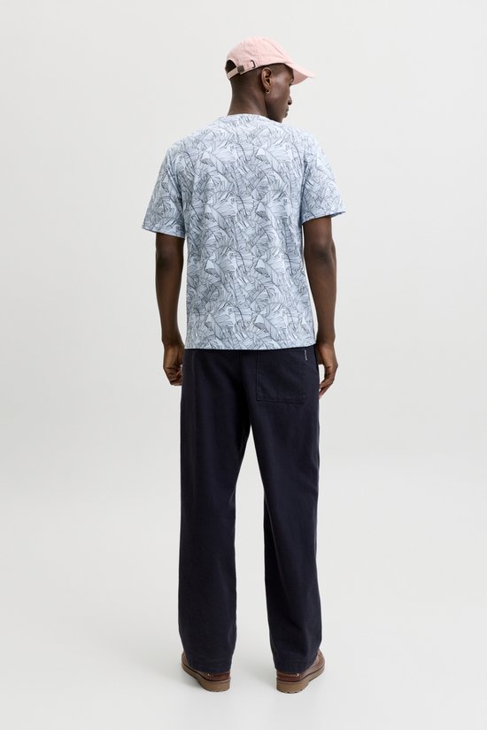 Man van achteren gezien, draagt een lichtblauwe T-shirt met bananenbladerenprint en donkerblauwe broek.