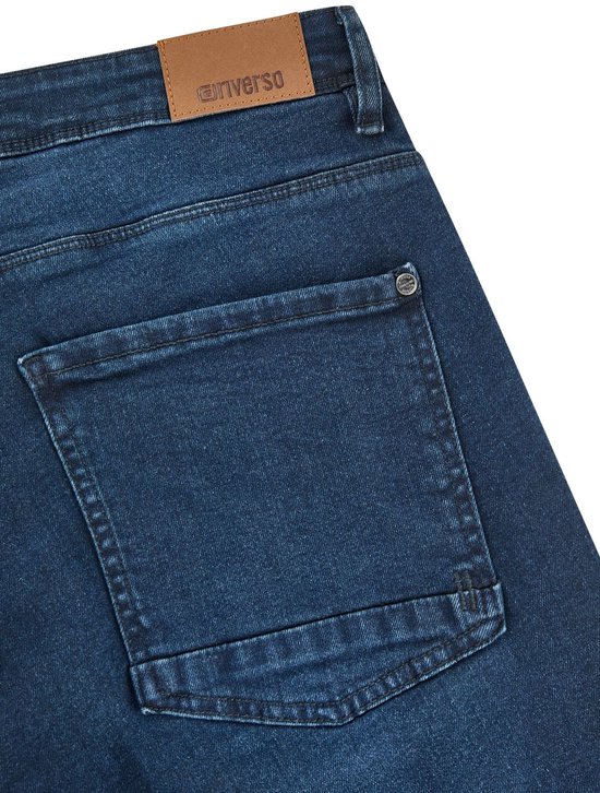 Detail van de achterkant van een donkerblauwe denim jeans met twee achterzakken en een bruin Riverso label.