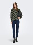 Model draagt een groene trui met zwarte chevron-strepen en donkere jeans.