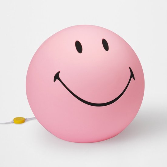 Lampe smiley rose avec yeux et bouche noirs.