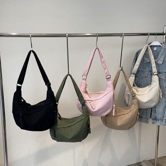 Collectie van vier corduroy crossbodytassen in zwart, groen, roze en beige, hangend aan een kledingrek.