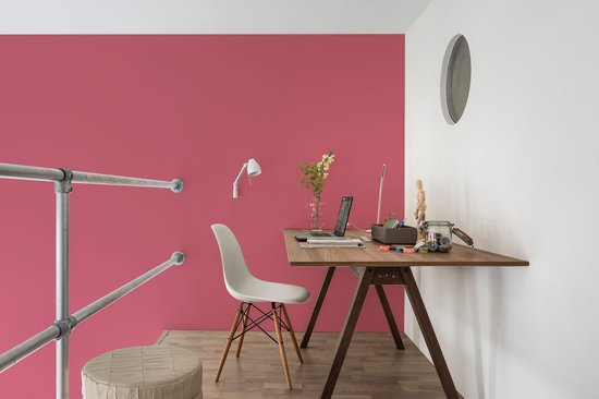 Een werkkamer met een roze muur, een houten bureau met laptop, witte stoel, en een roestvrijstalen leuning.