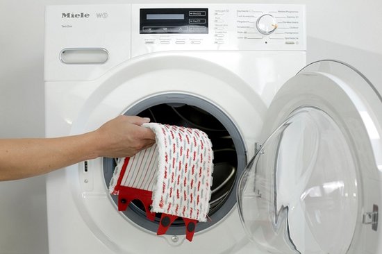 Main place une mop Vileda Ultramax Turbo XL rouge et blanche dans une machine à laver Miele.