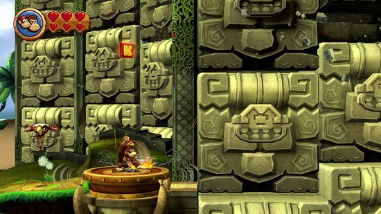 Donkey Kong sur une plateforme dans une jungle avec des sculptures en pierre et une pièce K.