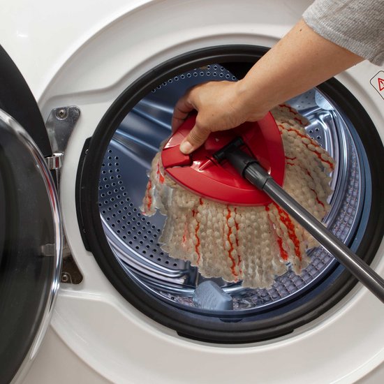 Hand plaatst de rode mopkop met witte en rode draden in een wasmachine.