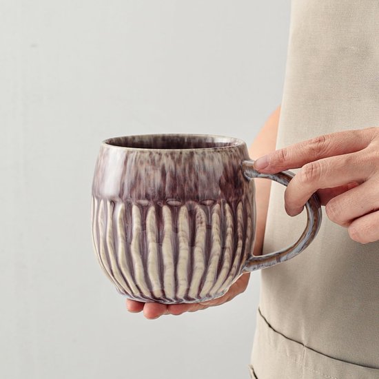 Tasse violette à côtes verticales et finition brillante, tenue par une personne.