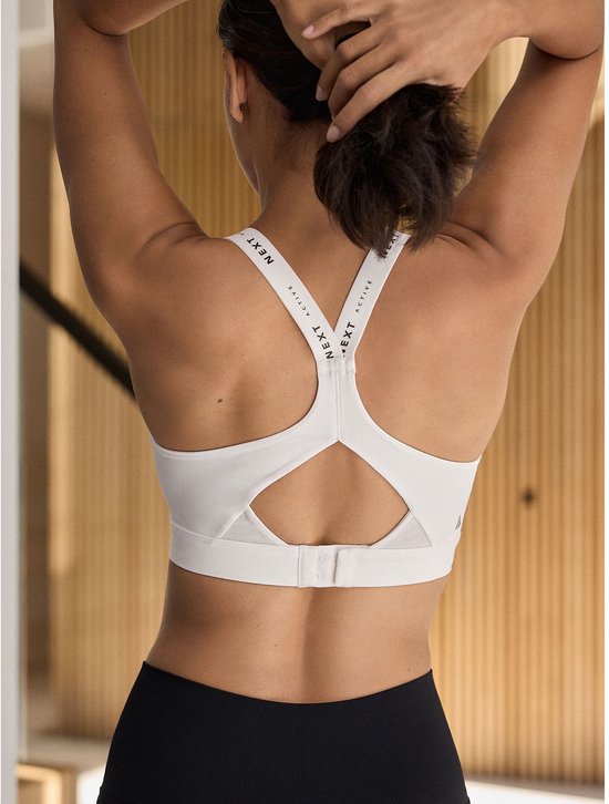 Achterkant van een vrouw in een witte sportbeha met merkdetails op de bandjes.