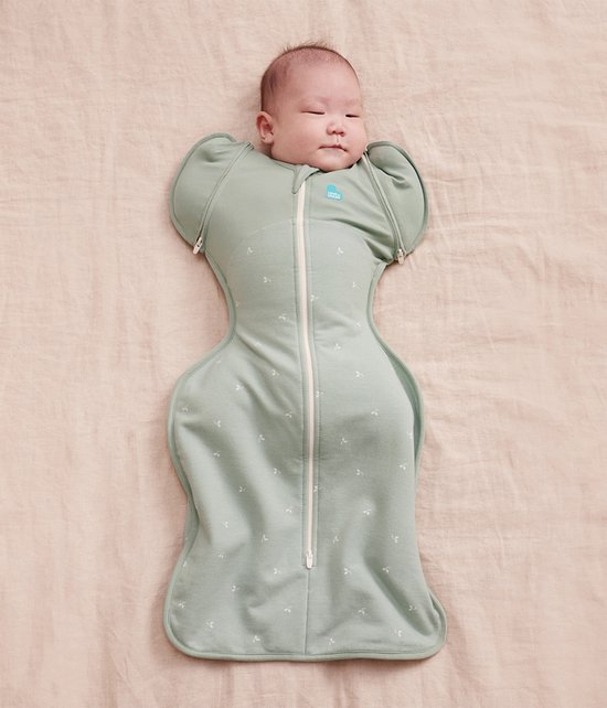 Baby in sagegroene slaapzak met takjesprint en rits, armen omhoog.