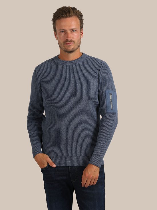 Man met donkerblauw gemêleerde trui met ronde hals, verticale ribbels en een opgestikte zak met ritssluiting op de linker mouw.