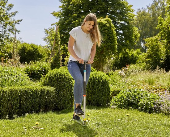 Vrouw met gestreept shirt en jeans onkruid wippend in een tuin met GARDENA onkruidsteker.