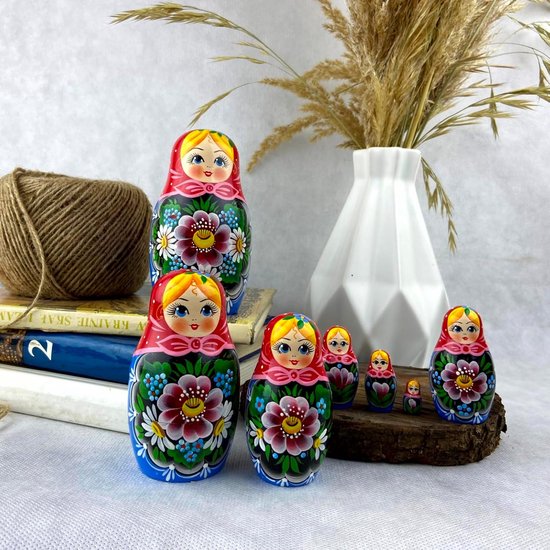Zeven handgeschilderde Russische nestpoppen met bloemenpatronen, op een houten plak, met boeken en een bol touw.
