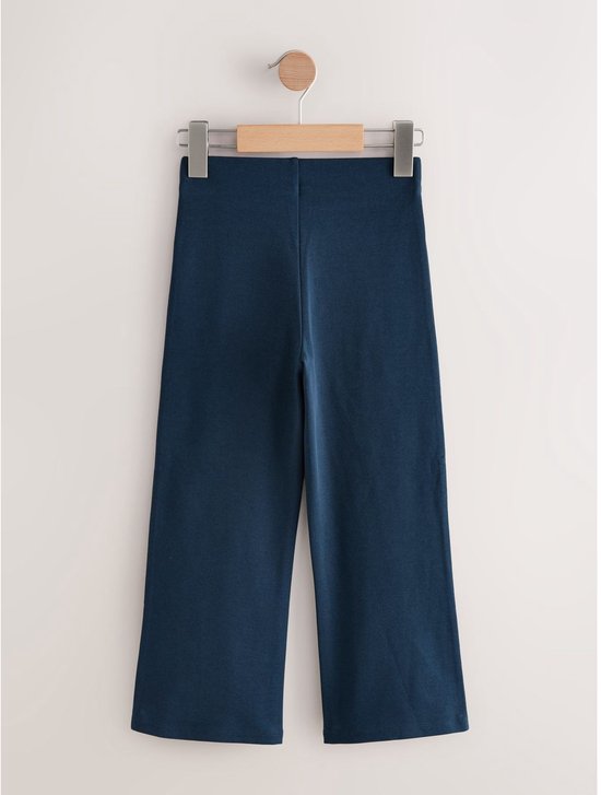 Donkerblauwe, wijde broek met elastische tailleband, hangend aan een kledinghanger.