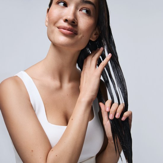 Model met lang, donker, nat haar dat haar lokken vasthoudt.