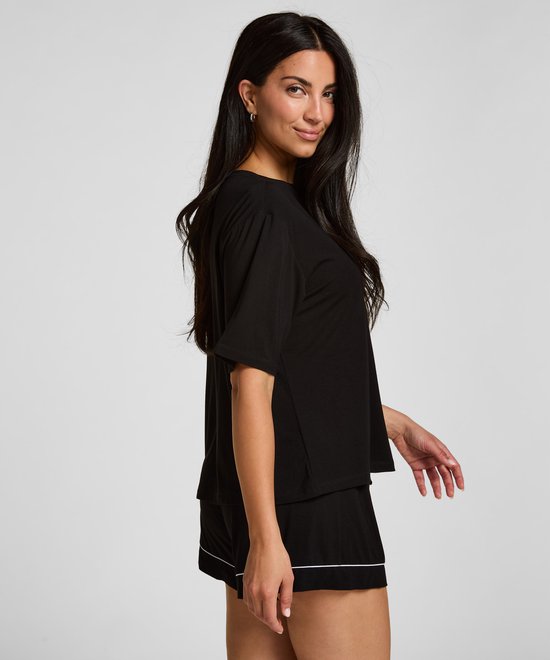 Vrouw in zwart pyjamashirt en korte broek met witte bies.