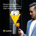 Man bij deurbel met telefoon, Varta knoopcelbatterijen boven gele driehoek. Aanbevolen voor smart devices.