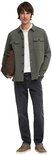 Man in olijfgroene utility blouse, wit poloshirt, grijze jeans, bruine tas en sneakers.