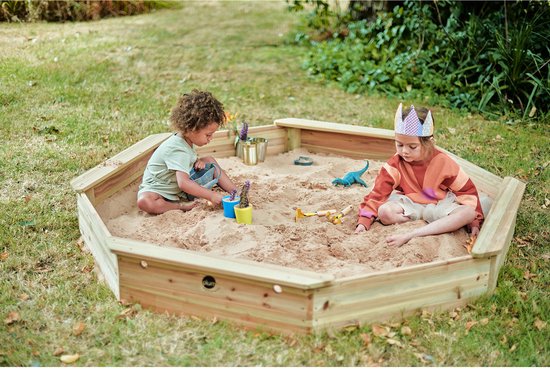 Zes kinderen spelen in de zeshoekige zandbak met zand en speelgoed. Een kind draagt een kroon.