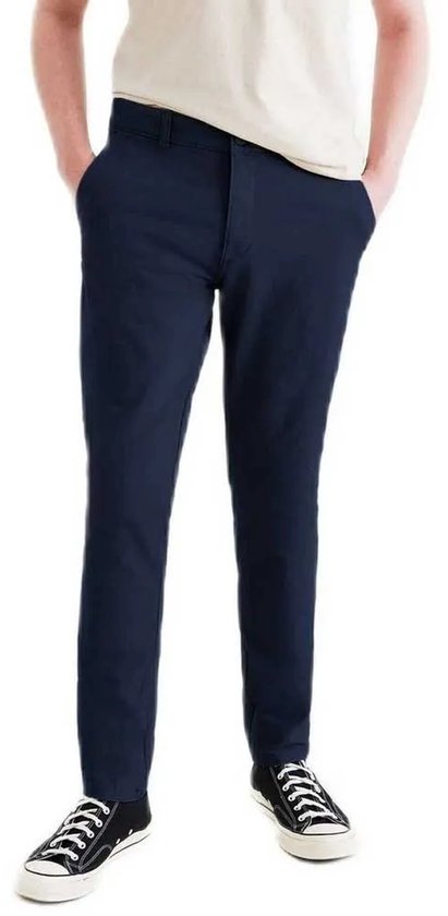 Man draagt een marineblauwe skinny fit chino met handen in de zakken en zwarte sneakers.