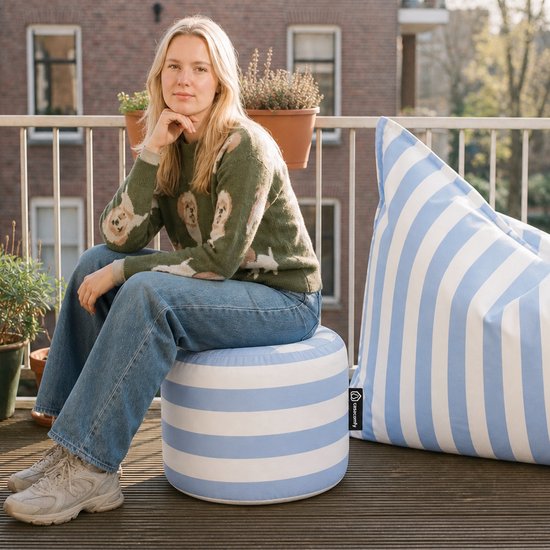 Vrouw zittend op een blauwe en witte gestreepte poef naast een grote beanbag.