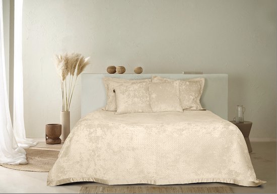 Een beige bed met twee beige sierkussens met een reliëf ruitpatroon, gedrapeerd op het bed.