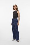 Model draagt een donkerblauwe, glanzende, geplooide broek met wijde pijpen.