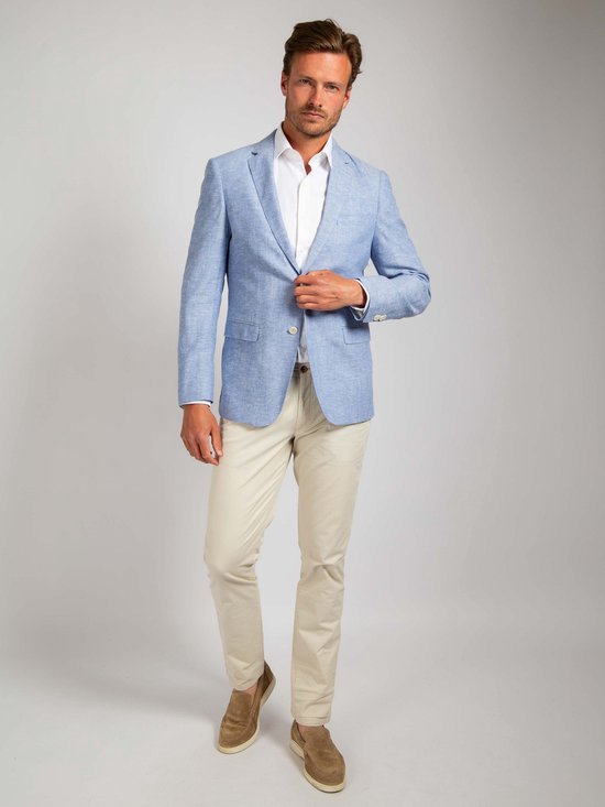 Man met lichtblauwe linnen blazer, wit overhemd en beige broek. Blazer is open en hij houdt de revers vast.