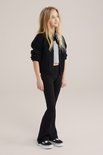 Meisje met lang blond haar draagt een zwarte flared legging, een grijs T-shirt en een zwart gebreid vest.