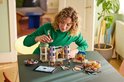 Vrouw in groene coltrui bouwt aan het LEGO Disney Belle en het Beest Kasteel.